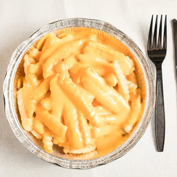Cheesy fries in a foil container with a black fork and knife on a white tablecloth.