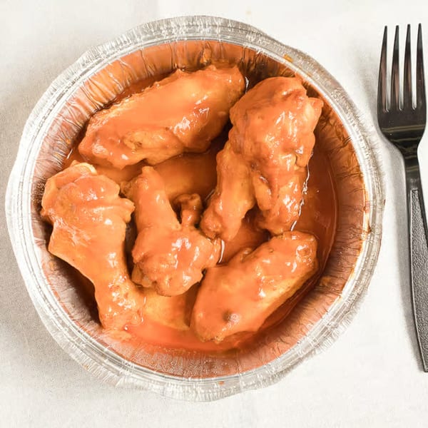Anthony's Pizza buffalo wings in a foil container with a fork on a white tablecloth.