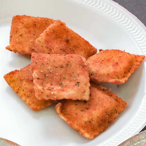 A white plate holds several golden-brown toasted ravioli, sprinkled with herbs and seasoning.